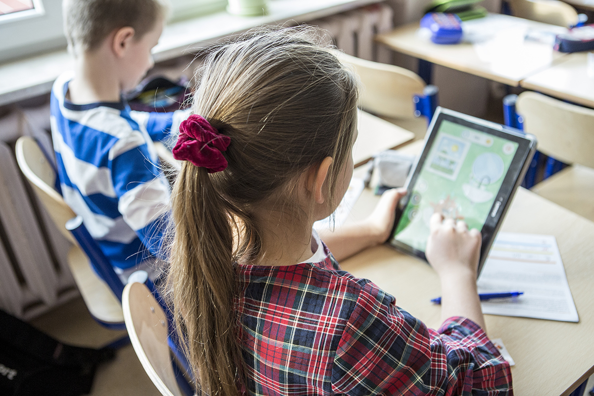 Dziewczynka siedząca obok chłopca patrząca się w ekran tableta