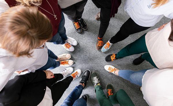Zdjęcie butów osób stojących blisko siebie w kółku z pomarańczowymi sznurówkami