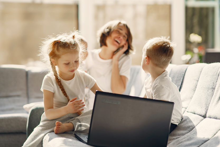 Laptop przed którym siedzi kobieta z trojgiem dzieci
